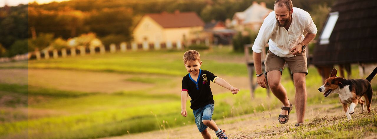 Father and young son running on grass with a dog